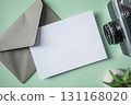 Empty white blank greeting or invitation card, envelope, vintage camera, cactus on green background. 131168020