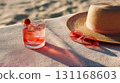 Strawberry cocktail on beach towel, cocktail chilled with ice beside sunhat and pink sunglasses, soft afternoon light and long shadows create leisurely mood, cocktail invites relaxed beach day vibe 131168603