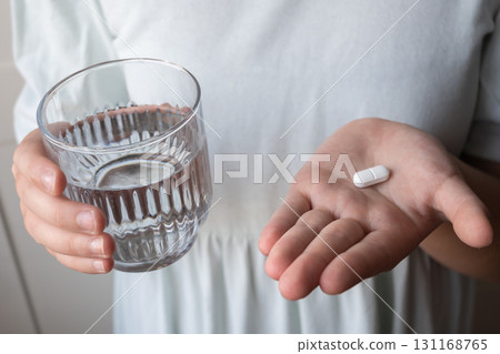 Pill and glass with water in the hand of child. Healthcare from pharmacy. Kid sit at home because of illness. Pill and glass with water in the hand of child. Healthcare from pharmacy. Kid sit at home because of illness. 131168765