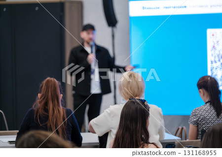 Presenter speaks at conference as audience listens in modern meeting room with blue screen Presenter speaks at conference as audience listens in modern meeting room with blue screen 131168955