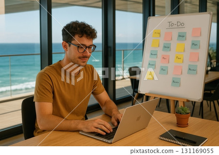 Man working on laptop with to-do board by ocean view in modern office setting 131169055