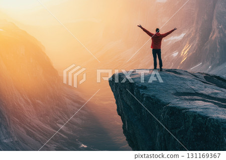 person standing at edge of cliff with arms raised, enjoying breathtaking view of valley at sunset. warm colors create sense of freedom and adventure 131169367