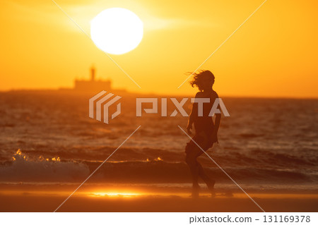 Woman dancing on the beach at sunset with lighthouse in background Woman dancing on the beach at sunset with lighthouse in background 131169378