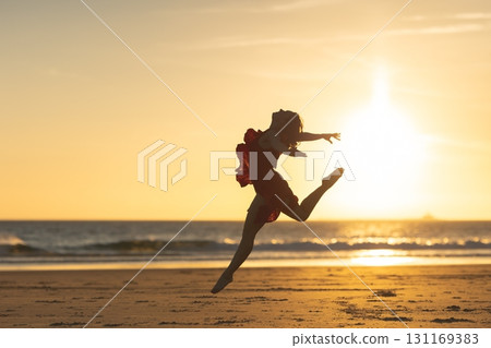 Ballerina jumping on the beach at sunset, embracing freedom and dance 131169383