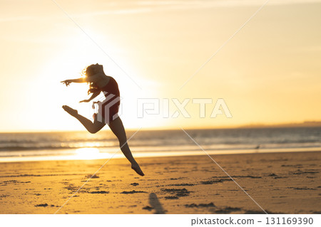 Ballerina performing graceful jump on beach at sunset 131169390