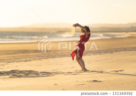 Dancer raising sand on beach at sunset with ocean waves 131169392