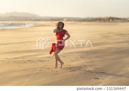 Dancer wearing red dress performing on sandy beach at sunset 131169447