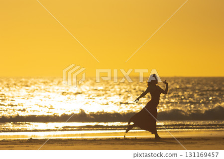 Female dancer performing on the beach at sunset, creating a stunning silhouette against the golden sky 131169457