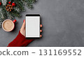 festive smartphone held in hand, surrounded by Christmas decorations, cup of coffee, and pine branches, creating cozy holiday atmosphere 131169552