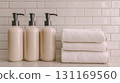 Elegant bathroom countertop with three cream colored bottles and stacked white towels, creating serene and organized atmosphere 131169560