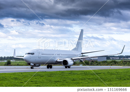 White passenger airplane taxiing at the taxiway at the airport in cloudy weather White passenger airplane taxiing at the taxiway at the airport in cloudy weather 131169666