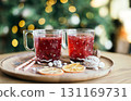 Two glasses of mulled wine with a festive pattern are served on a wooden tray with dried oranges and nuts, against a background of Christmas lights. 131169731