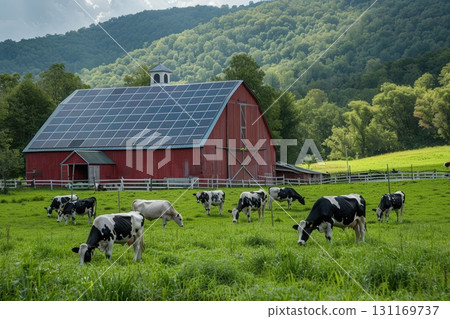 A red barn with solar panels on its roof is situated in a green pasture where a herd of black and white cows graze, with lush, forested hills in the background. 131169737