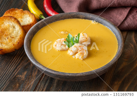 Rustic shrimp bisque with toasted baguette slices beside clay bowl 131169793