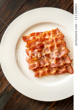 Crispy fried bacon slices neatly arranged on simple white serving plate Crispy fried bacon slices neatly arranged on simple white serving plate 131169803