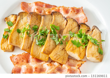 Fried eryngii mushrooms served with crispy bacon slices on white plate Fried eryngii mushrooms served with crispy bacon slices on white plate 131169811