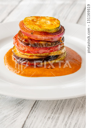 Elegant vertical ratatouille tower layered with colorful vegetables on white plate Elegant vertical ratatouille tower layered with colorful vegetables on white plate 131169819