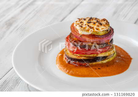 Elegant vertical ratatouille tower layered with colorful vegetables on white plate 131169820