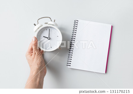 Alarm clock in woman hand and empty sheet blank on gray background. Daily routine. View from above. Copy space. 131170215