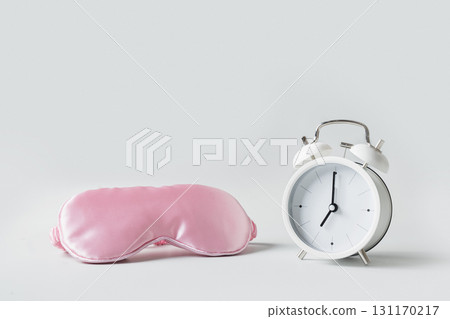 Soft contoured eye mask for comfortable sleep. Pink mask and white alarm clock on gray background. Concept of sleep, insomnia, health care, daily routine and circadian rhythms. Can't fall asleep. Soft contoured eye mask for comfortable sleep. Pink mask and white alarm clock on gray background. Concept of sleep, insomnia, health care, daily routine and circadian rhythms. Can't fall asleep. 131170217