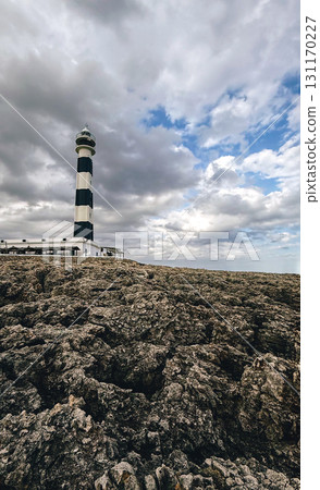 Tall black and white lighthouse standing on rocky shore 131170227