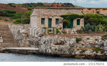 Old stone house with green doors and tiled roof perched on rocky coastline Old stone house with green doors and tiled roof perched on rocky coastline 131170231