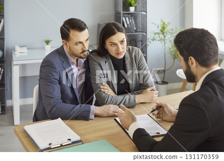 Businesswoman and businessman sitting in real estates office at desk, having talk with agent Businesswoman and businessman sitting in real estates office at desk, having talk with agent 131170359