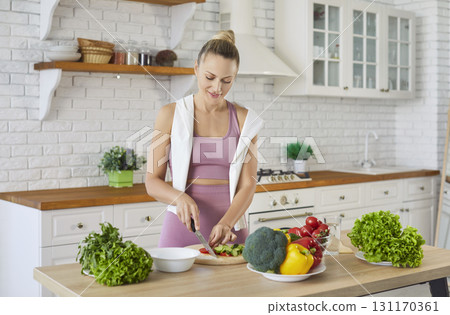 Modern indoor kitchen, happy fit woman wearing fitness attire standing and cutting vegetables Modern indoor kitchen, happy fit woman wearing fitness attire standing and cutting vegetables 131170361