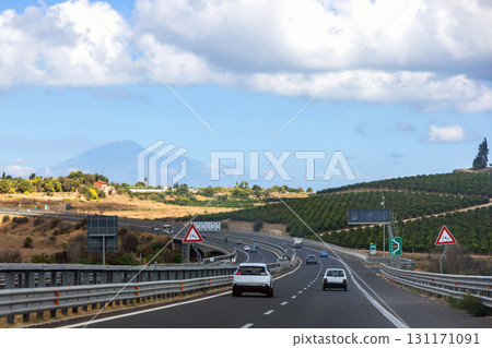 Picturesque Sicilian highway with cars, volcanic backdrop, and clear weather Picturesque Sicilian highway with cars, volcanic backdrop, and clear weather 131171091