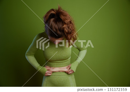 Woman in green assesses her lower abdomen 131172359