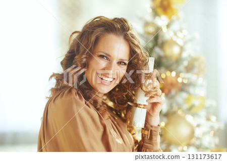 Woman Holds Christmas Cracker by Festive Tree 131173617