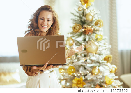 Woman with Golden Laptop by Snowy Christmas Tree 131173702