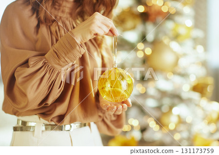 Woman\'s Hands Adorn Christmas Tree with Gold Bauble 131173759