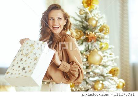Cheerful Woman Holding Open a Festive Gift Bag by Flocked Tree Cheerful Woman Holding Open a Festive Gift Bag by Flocked Tree 131173781