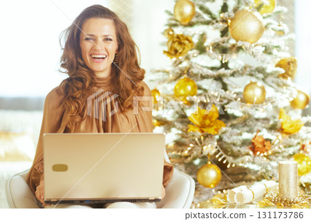 Smiling Woman Holding Gold Laptop by Christmas Tree 131173786