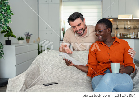 Happy multi-ethnic couple reading good news at home sitting on the sofa 131173894