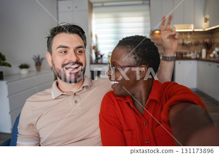 Happy multi-ethnic couple taking a selfie on the sofa at home 131173896