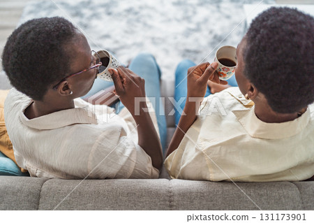 Two black women relaxing on sofa, drinking coffee at home Two black women relaxing on sofa, drinking coffee at home 131173901