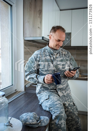 Soldier enjoying a coffee break and checking his phone in the kitchen 131173926
