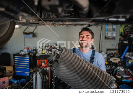 Mechanic smiling and holding a car radiator in a garage 131173955
