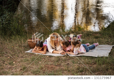Mother Lying with her Three Daughters by the River Having a Picnic 131173967