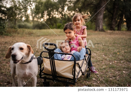 Dog pulling wagon with three little girls in a park 131173971