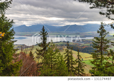 The Liptovska Mara dam in northern Slovakia, Europe. Overlooking a scenic lake surrounded by lush green hills and majestic mountains under a cloudy sky. 131174497