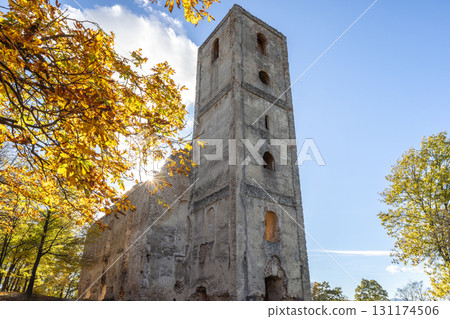 The Katarinka, ruins of a Franciscan monastery and church in Slovakia, Europe. Towering stone structure stands amidst trees, sun shining through autumnal foliage against the bright sky. 131174506
