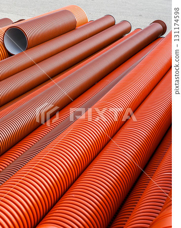 Stack of large orange corrugated plastic pipes at construction site for drainage and infrastructure 131174598
