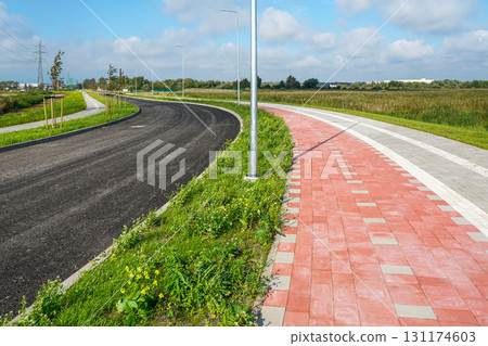Newly paved asphalt road with red brick bicycle lane and green grass under blue sky Newly paved asphalt road with red brick bicycle lane and green grass under blue sky 131174603