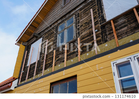 Old wooden house under renovation with new yellow siding and insulation installation process 131174610