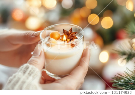 Cozy winter vibes: hands holding a lit candle near festive evergreen branch Cozy winter vibes: hands holding a lit candle near festive evergreen branch 131174923