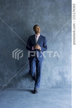 Man in suit standing against wall 131176303