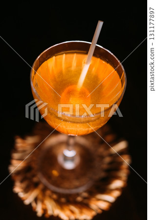 Exotic beverage. Sweet cocktail. Yellow liquid served with orange lollipop in wineglass. Caramel aroma flavor drink isolated on black. Exotic beverage. Sweet cocktail. Yellow liquid served with orange lollipop in wineglass. Caramel aroma flavor drink isolated on black. 131177897